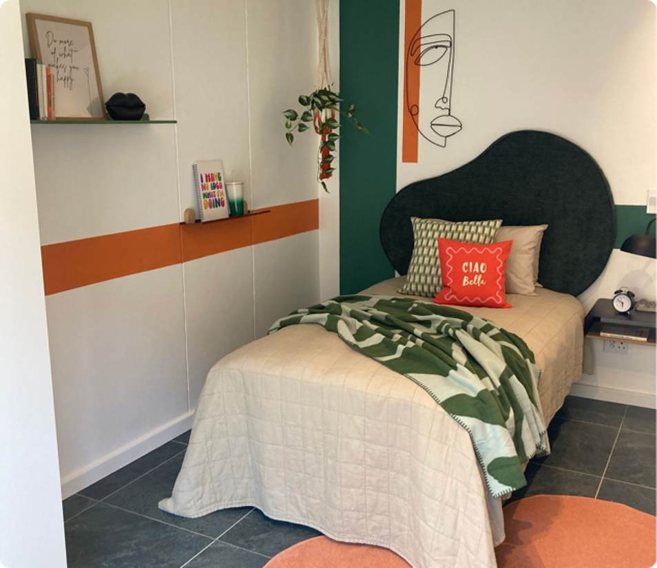 Main Road 2-bedroom room, angled bed with green throw and Ciao Bella cushion.