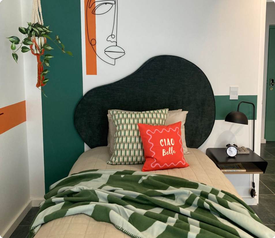 Main Road 3-bedroom room, frontal bed view with Ciao Bella cushion and green throw.