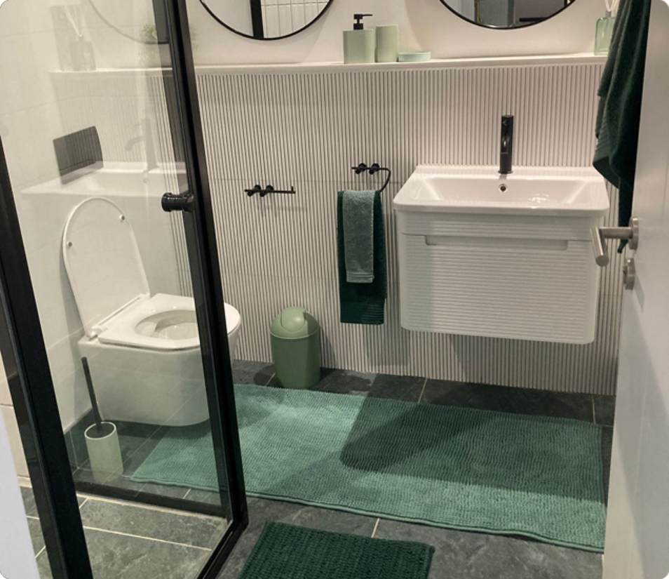 Main Road Standard Bachelor bathroom, glass shower, green mat and white sink.
