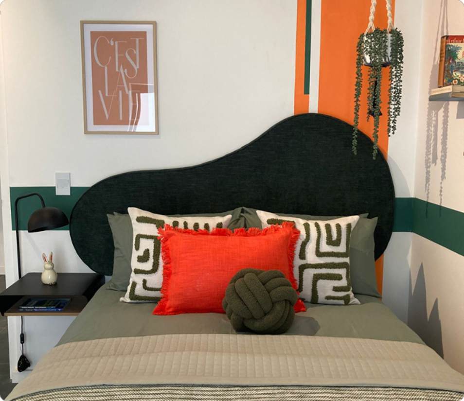 Main Road Standard Bachelor double bed, orange cushion and green headboard.